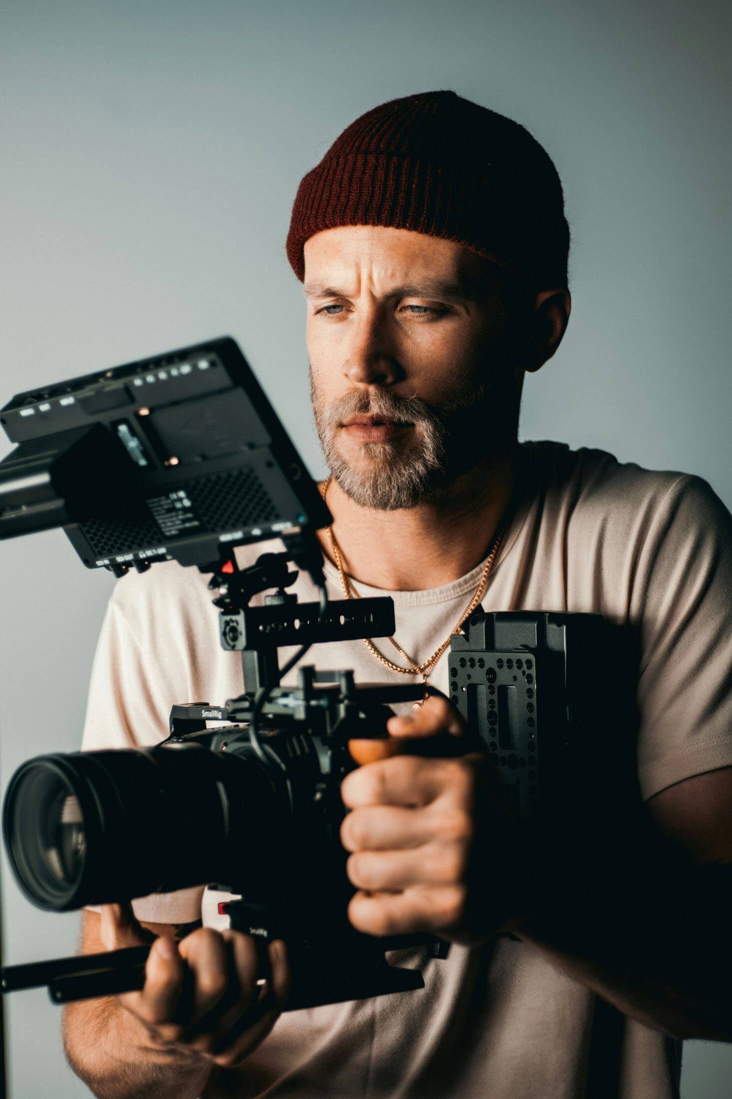 Närbild av person som håller en professionell videokamera med extern monitor, fotograferad i studiomiljö.