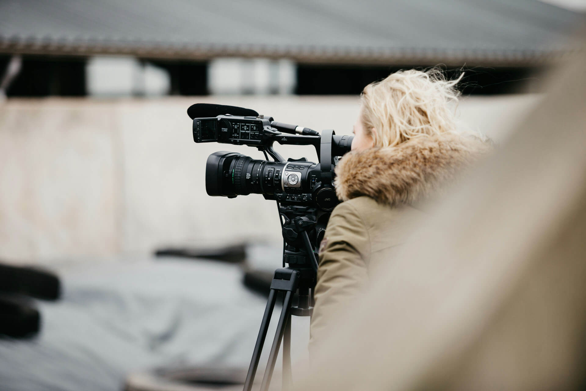Person använder en professionell videokamera på stativ utomhus, fokus på kamerautrustning och dokumentär fotografering i naturlig miljö.