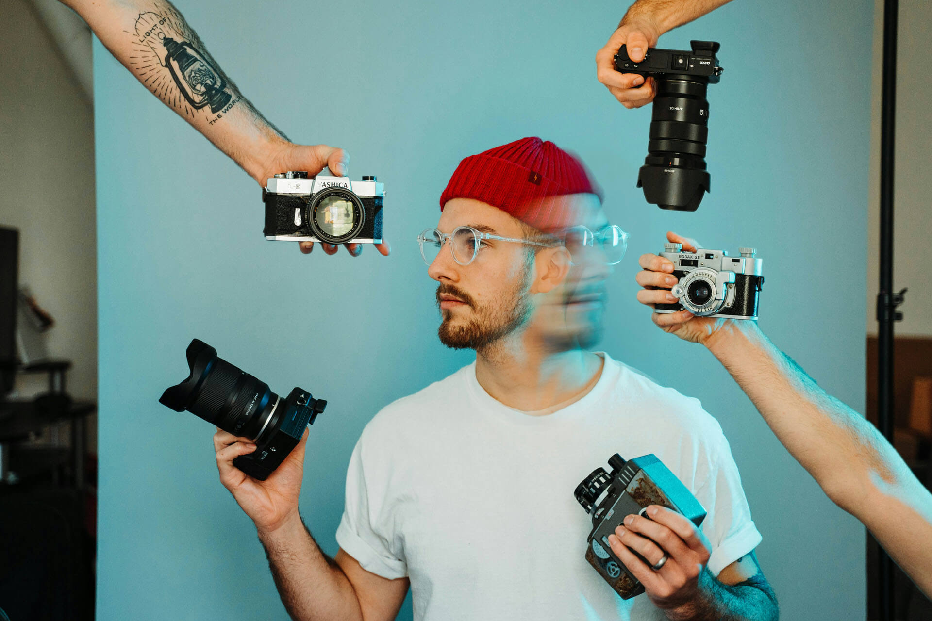 Person i studio omgiven av flera kameror som hålls upp runt omkring, med fokus på fotografisk utrustning och kreativ presentation.