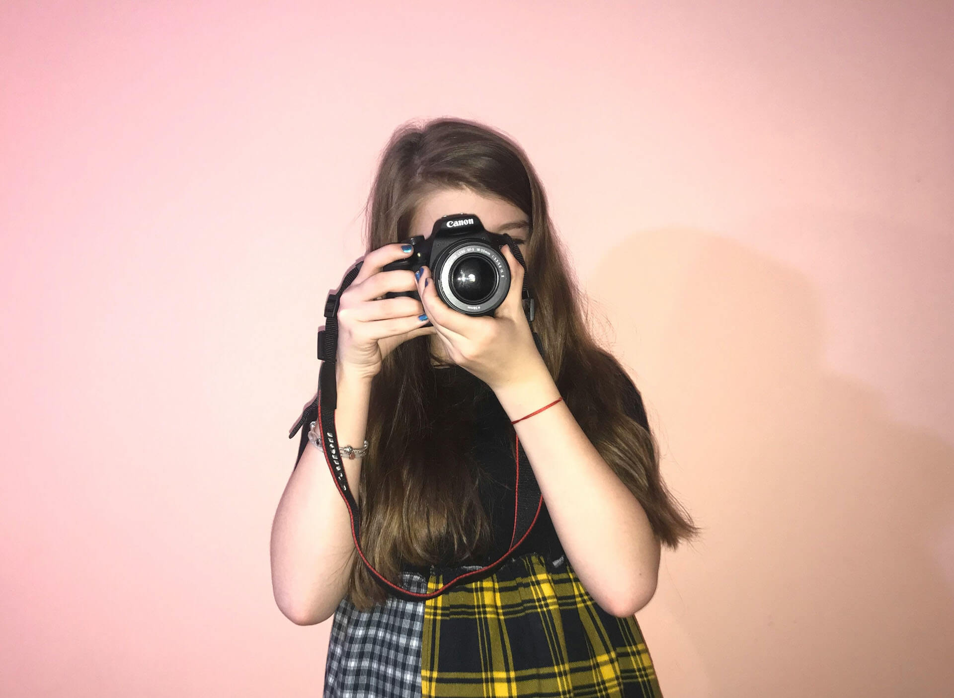 Person håller upp en systemkamera framför ansiktet mot enfärgad bakgrund, med fokus på fotografens utrustning.