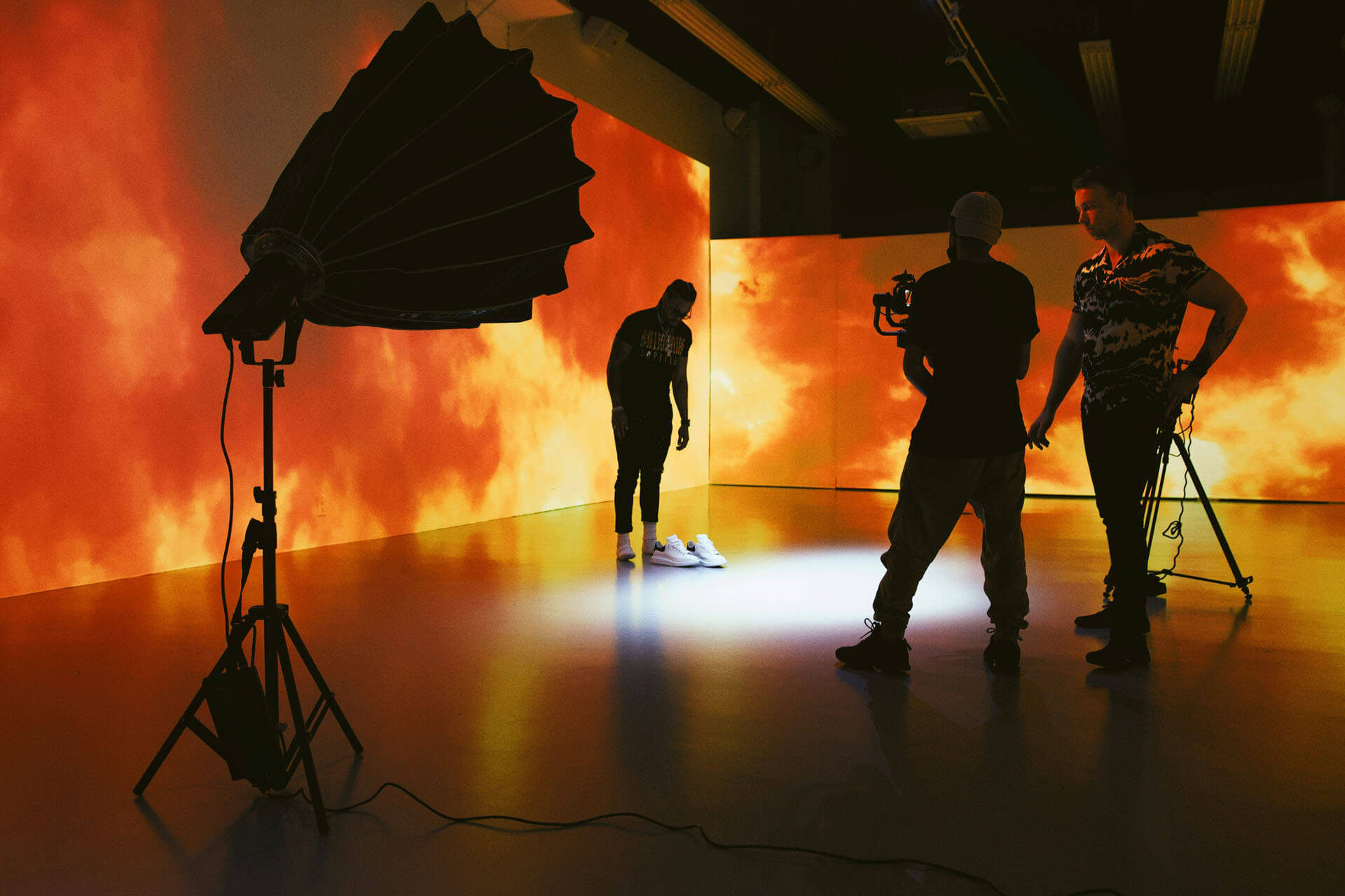 Filmteam arbetar i studio med stora skärmar i bakgrunden som visar eldliknande visuella effekter, där flera personer står med kamerarigg och ljusutrustning runt en inspelningsyta.