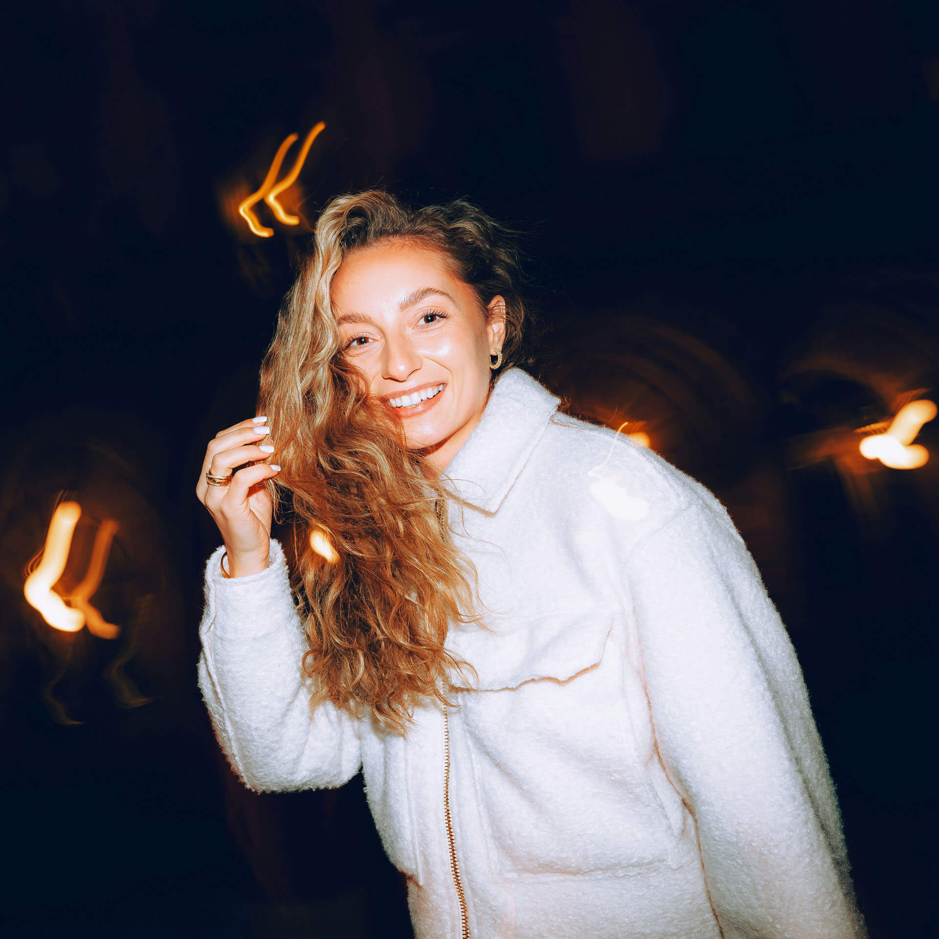 Modellfoto från TFP-fotografering utomhus i Stockholm där person i ljus jacka står mot mörk bakgrund med långa ljusspår. Den kreativa ljussättningen skapar ett dynamiskt porträtt för modellportfölj och marknadsföring.