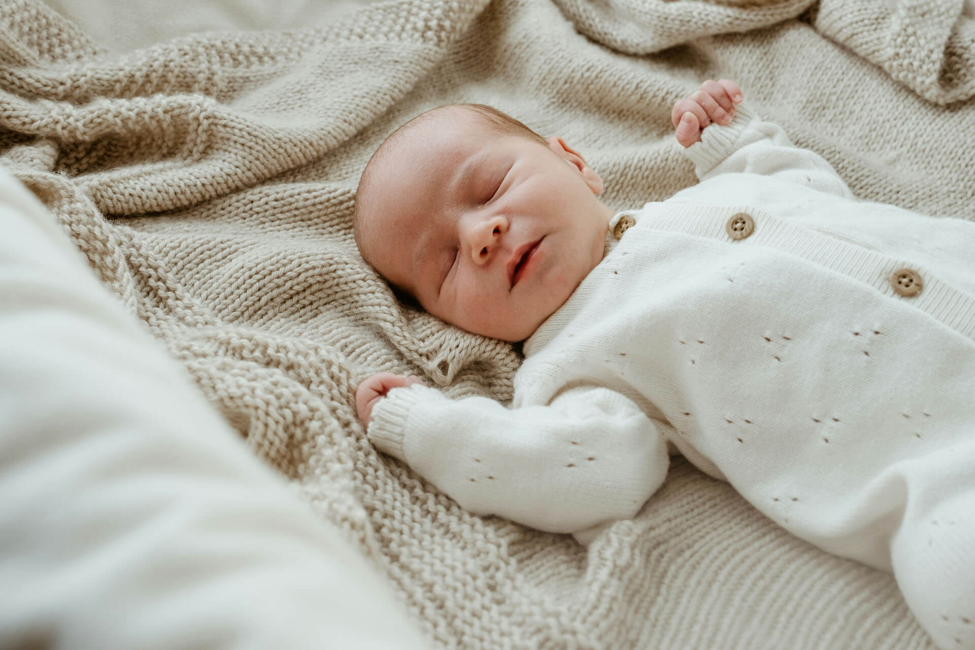 Sovande nyfödd bebis i vit stickad outfit på beige filt.