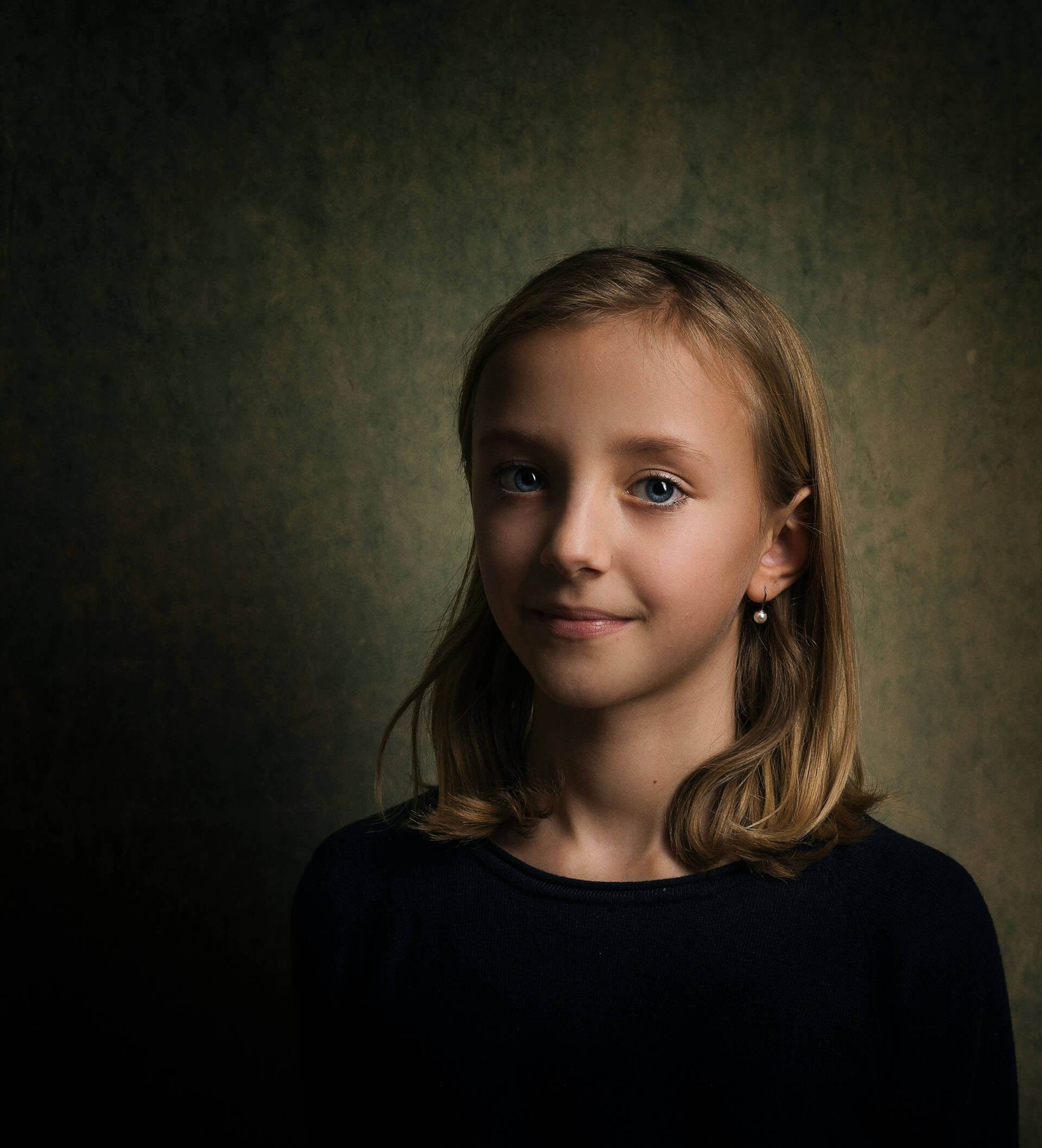 Porträtt av ett barn i studio taget av fotograf i Stockholm där barnets ansikte framträder i mjukt riktat ljus mot en mörkt tonad bakgrund med kort skärpedjup.