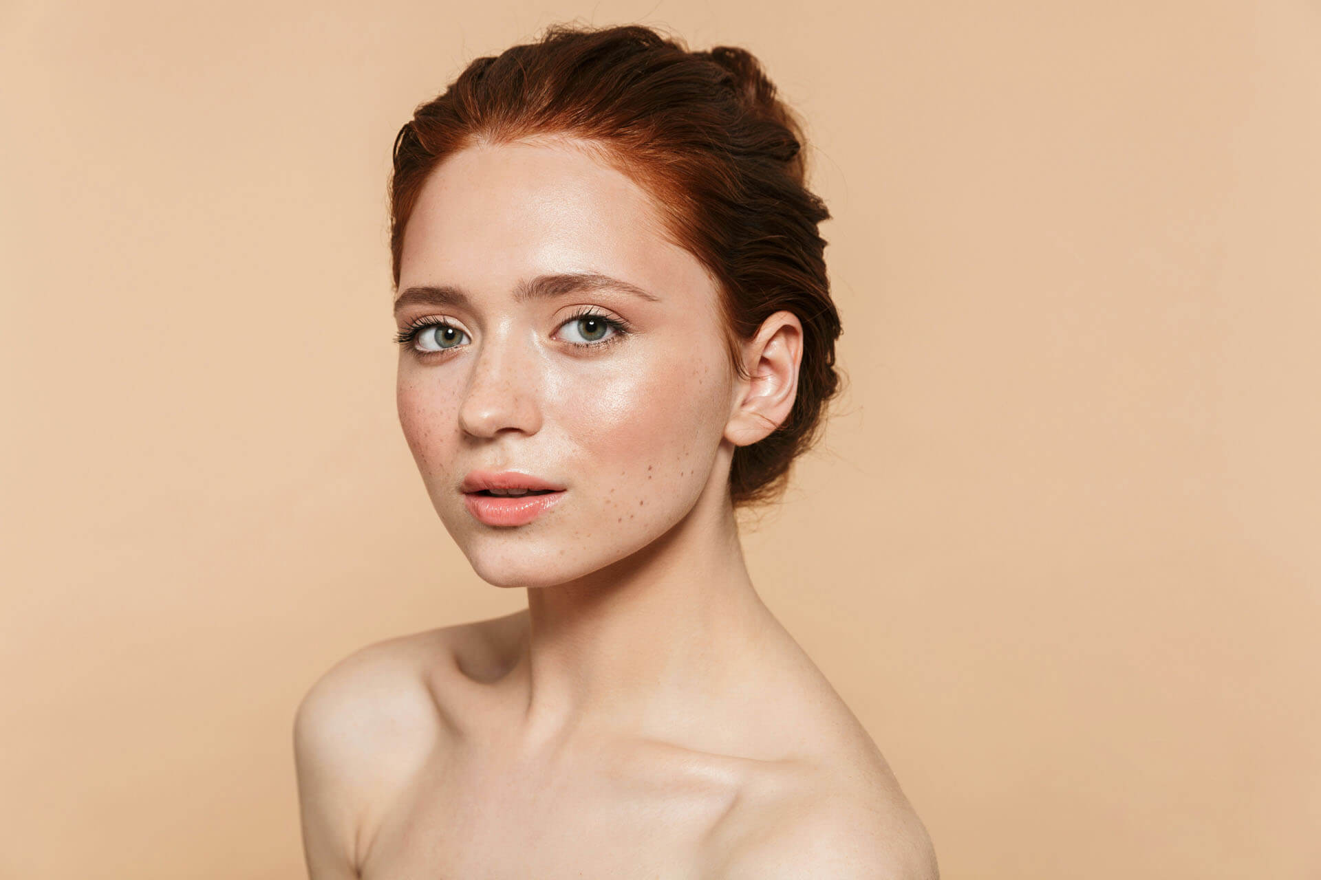 Porträtt från studiofotografering i Stockholm med naturlig hudtextur och fräknar mot varm beige bakgrund. Bilden visar professionell bildretuschering och färgkorrigering där hudtoner och detaljer bevaras på ett naturligt sätt.