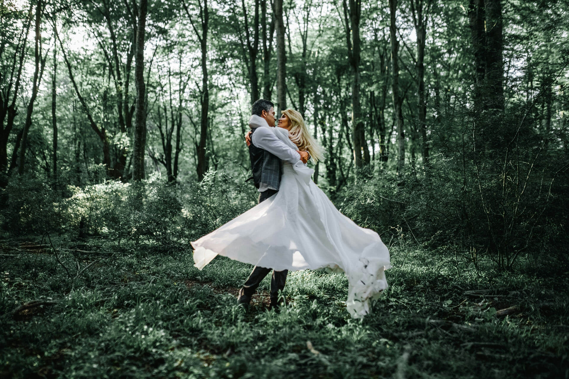 Brudpar dansar romantiskt i skogen medan brudens klänning virvlar i mjukt kvällsljus.