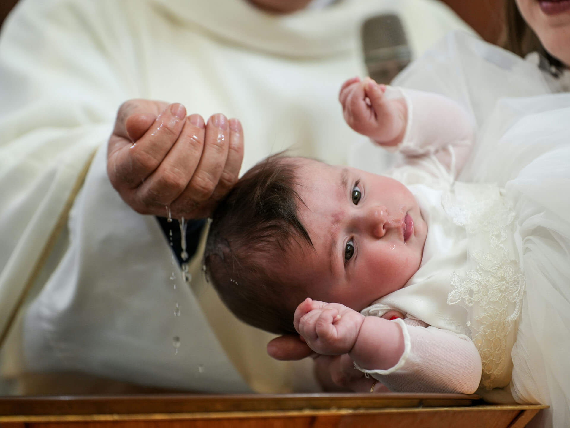 Präst häller dopvatten över bebis huvud under dopceremoni i kyrka.