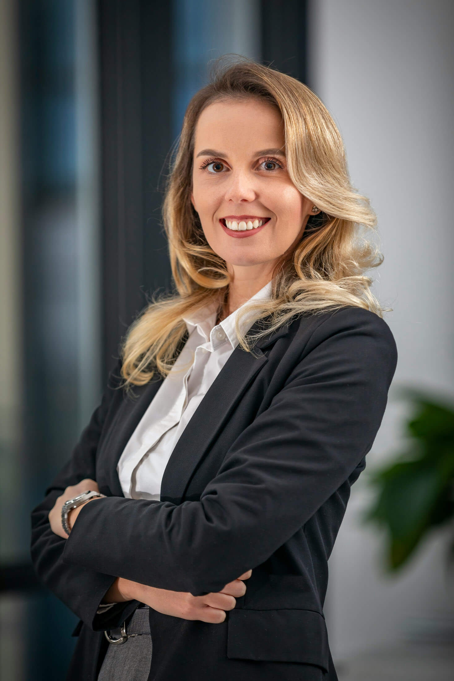 Fotograf i Stockholm tar bild av en kvinnlig entreprenör i kavaj och som står med armarna i kors och ler på ett kontor. Den mjuka bakgrundsoskärpan och den självsäkra posen skapar ett professionellt affärsporträtt.