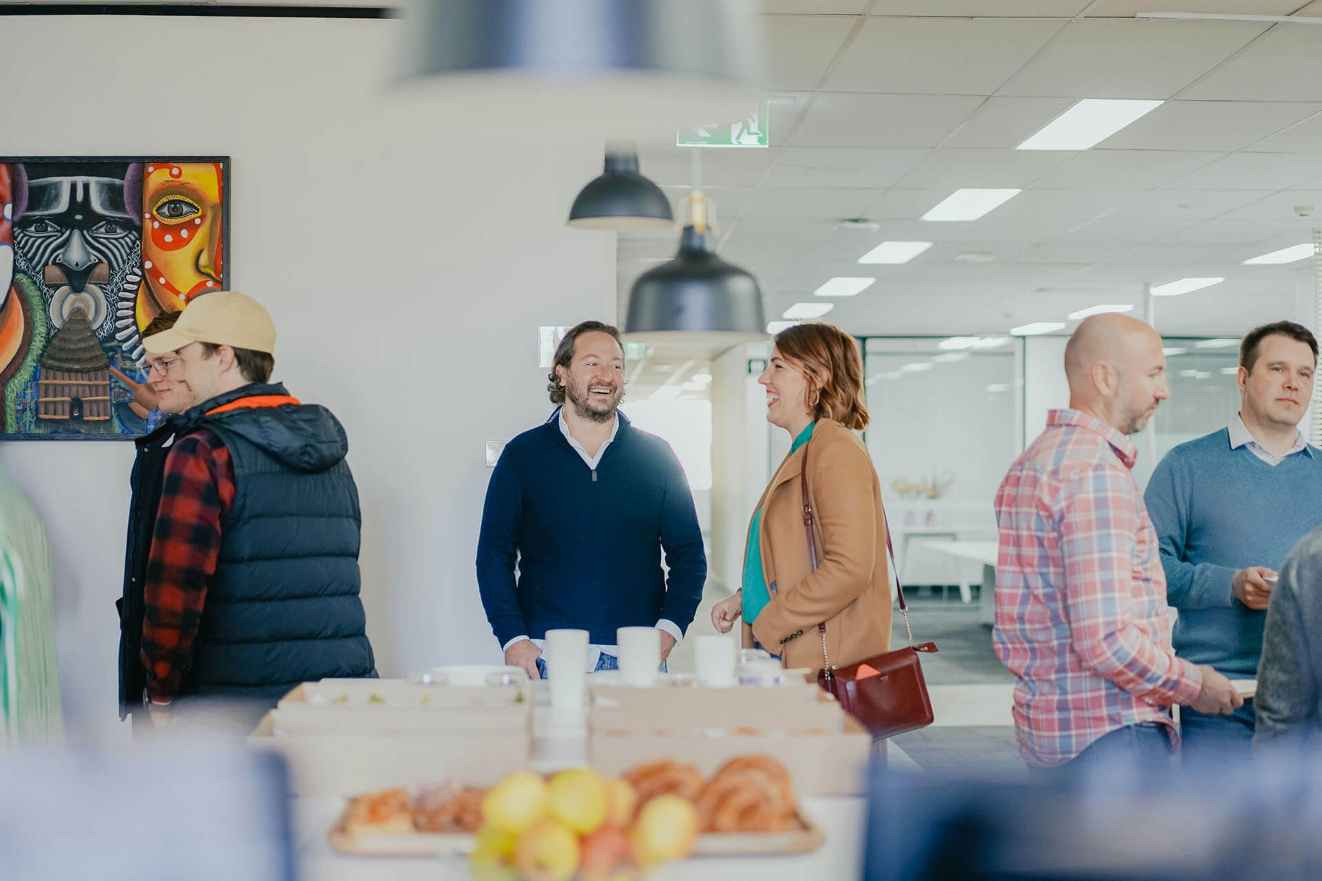 Personer minglar och samtalar i en ljus kontorsmiljö vid ett företagsevent med bord, lampor och konstverk i bakgrunden.