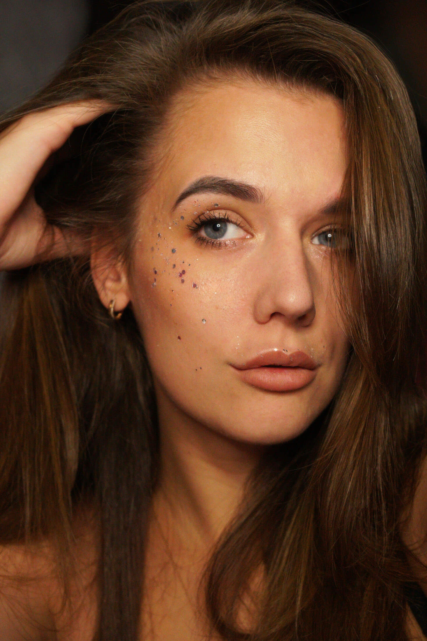 Bild från fotografering i Stockholm där person med långt hår poserar med handen i håret och tittar på sidan av kameran. Bilden visar professionell bildretuschering och färgkorrigering där hudtoner, makeup och hår framhävs med ett detaljrikt resultat.
