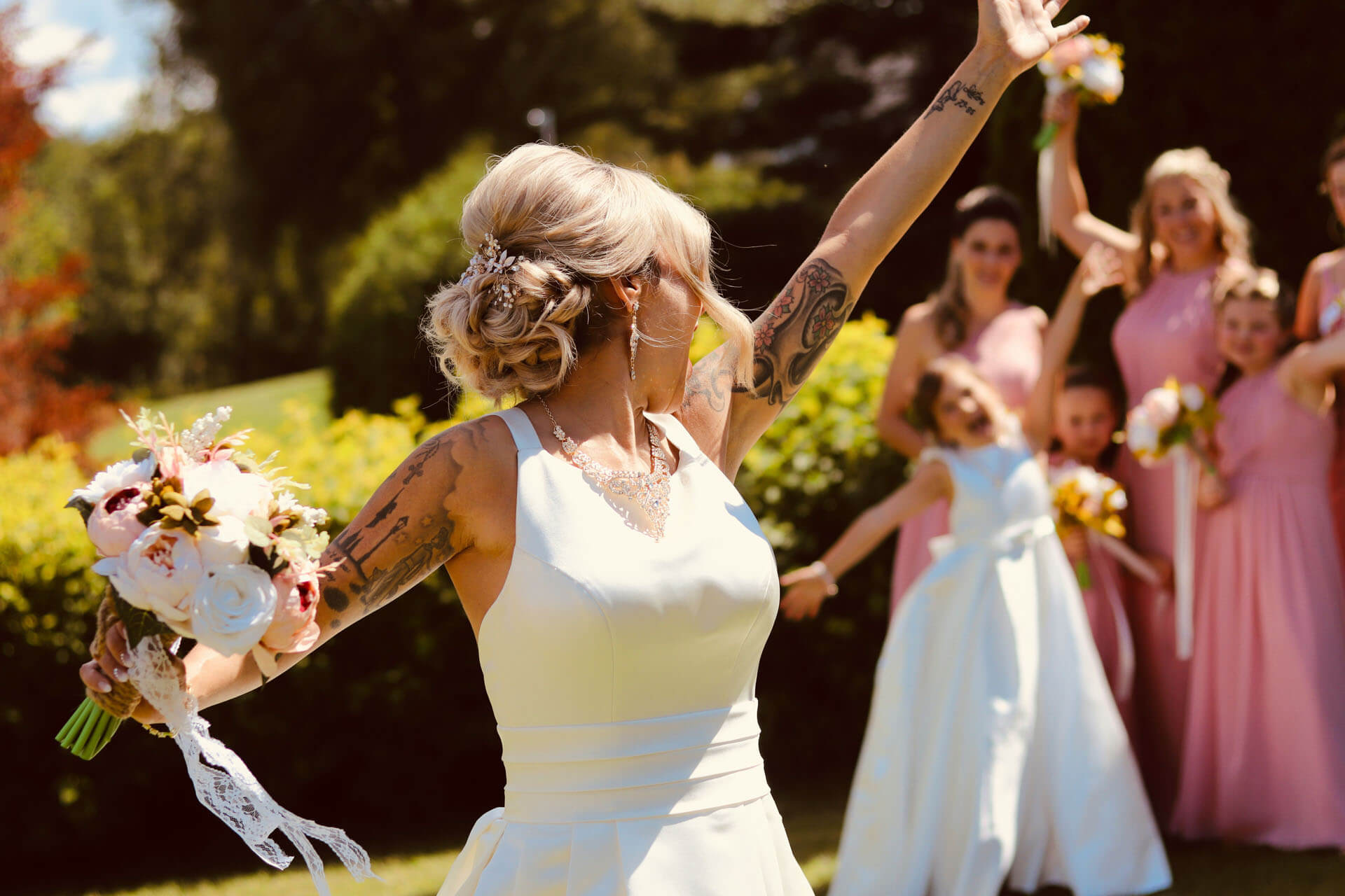  Brud med tatueringar kastar buketten bakåt till väntande brudtärnor under sommarbröllop.