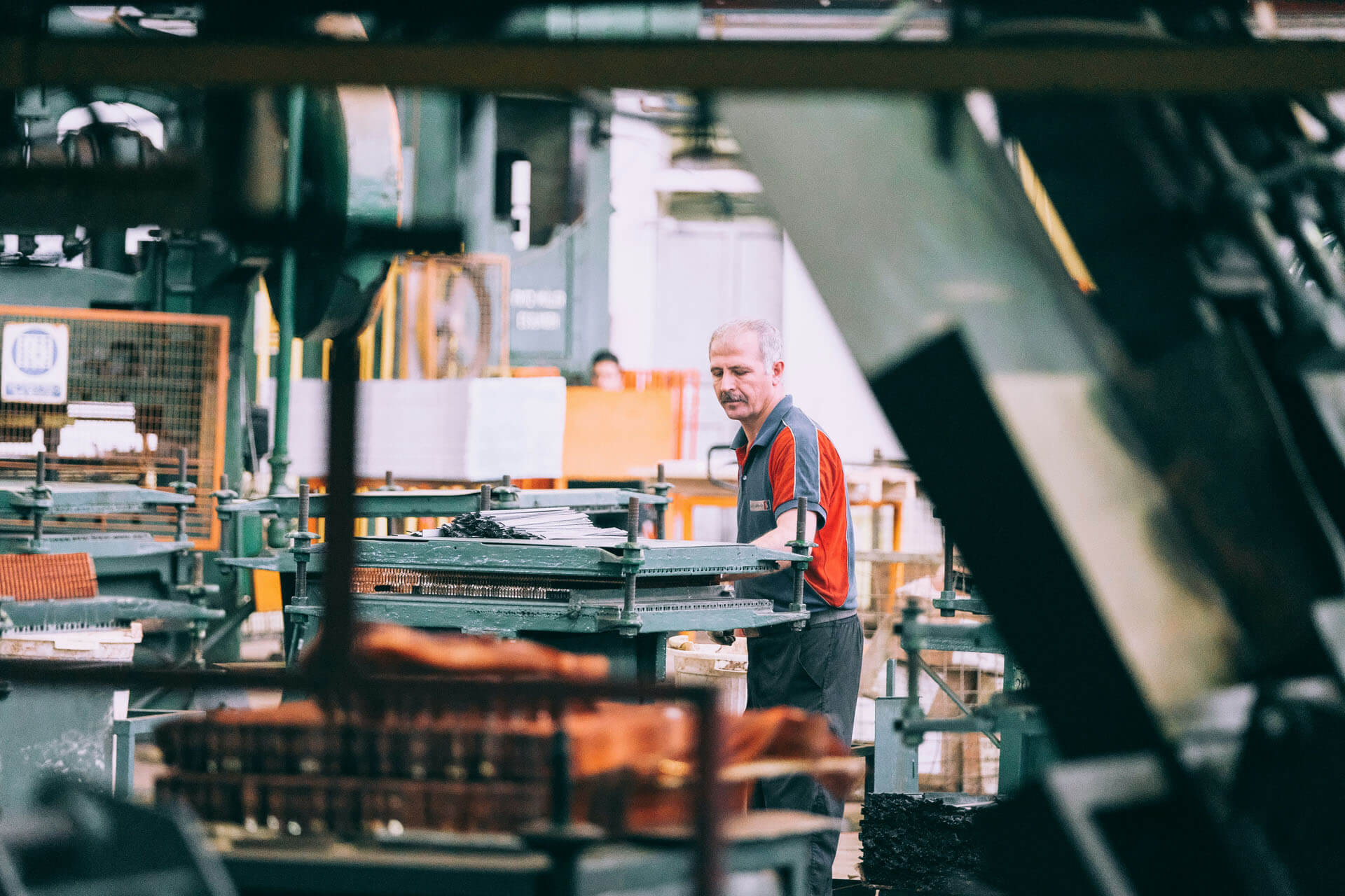 Företagsfoto taget av fotograf i Stockholm där en fabriksarbetare arbetar bland maskiner och produktionsutrustning i en industrimiljö. Bilden visar verksamhetsbilder från tillverkningsindustrin med fokus på produktion och arbetsprocesser.