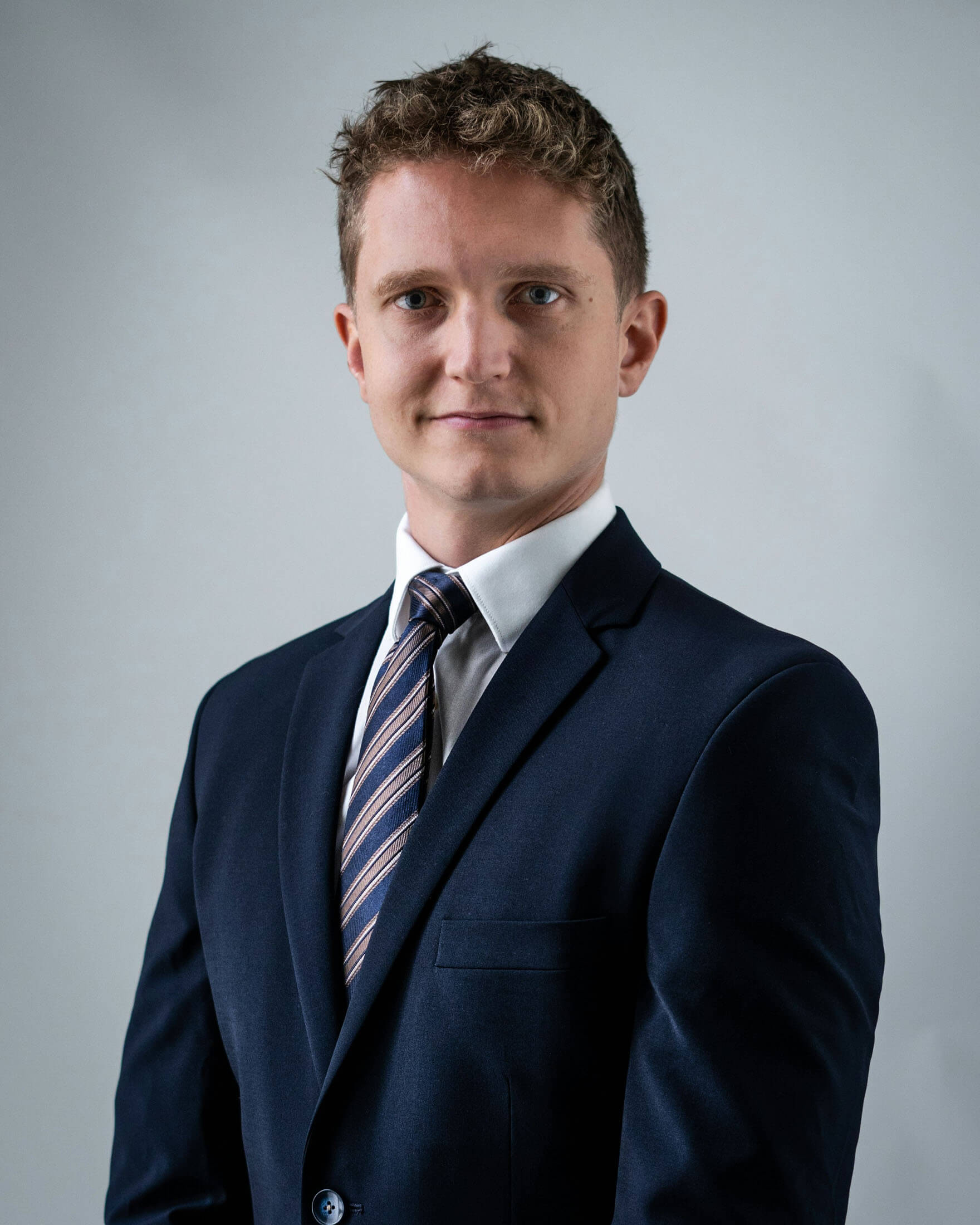 Personalfoto upp från midjan taget av företagsfotograf i Stockholm där person i kostym och slips fotograferas rakt framifrån med händerna hängandes på sidan mot en ljus bakgrund. Den jämna belysningen skapar ett klassiskt företagsporträtt.