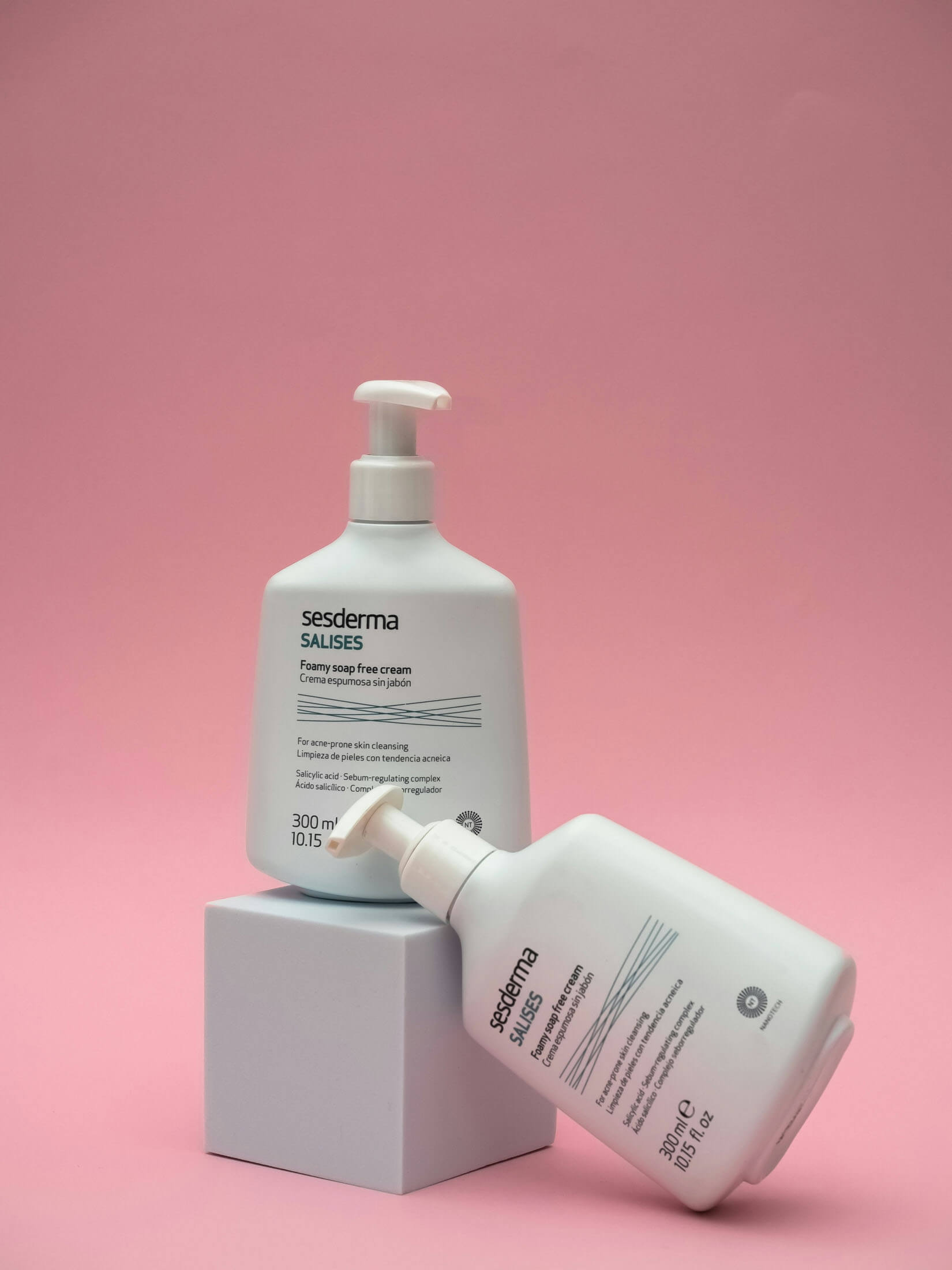 Produktfoto taget i Studio i Stockholm där två vita hudvårdsflaskor med pump är fotograferade mot en rosa bakgrund, ena står på en vit kub och den andra lutar mot samma kub. Den minimalistiska studiokompositionen framhäver produktdesign och förpackning för e-handel och marknadsföring.