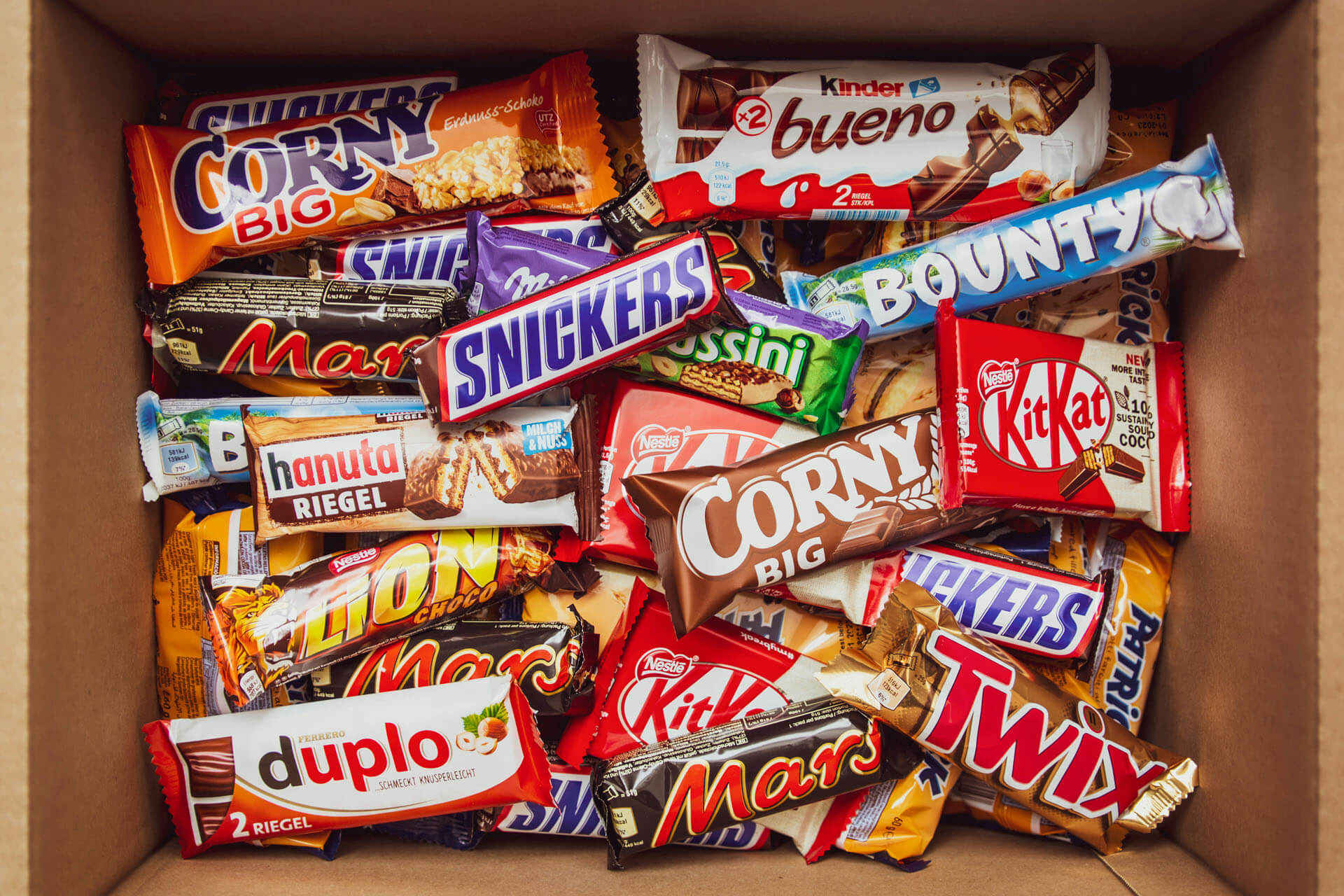Produktfoto taget av fotograf i Stockholm med en öppen kartong fylld med choklad- och godisförpackningar från olika varumärken. De starka färgerna och den täta kompositionen skapar en reklambild för marknadsföring och kampanjer.