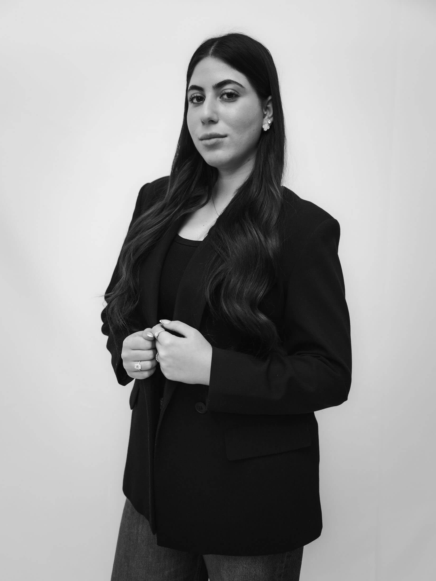 Svartvitt företagsporträtt taget av fotograf i Stockholm där person i kavaj med händerna på knäppningen står mot en ljus bakgrund. Den enkla kompositionen och jämna belysningen skapar ett professionellt personalfoto.