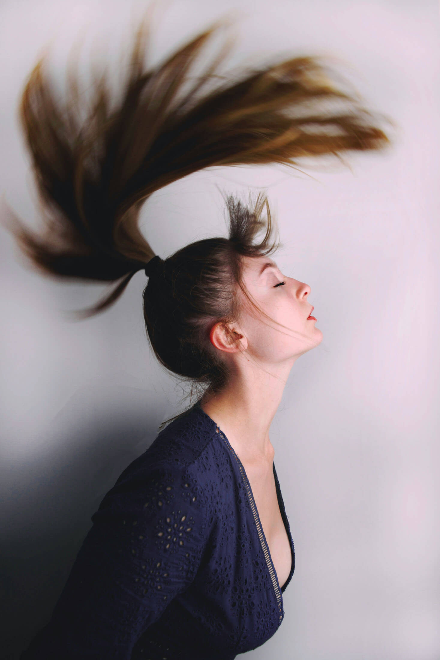 Porträttfotografering i studio där personen kastar bak huvudet och håret sveper genom luften. Bilden visar professionell fotoretuschering i Stockholm med fokus på rörelse, form och detaljrikedom.