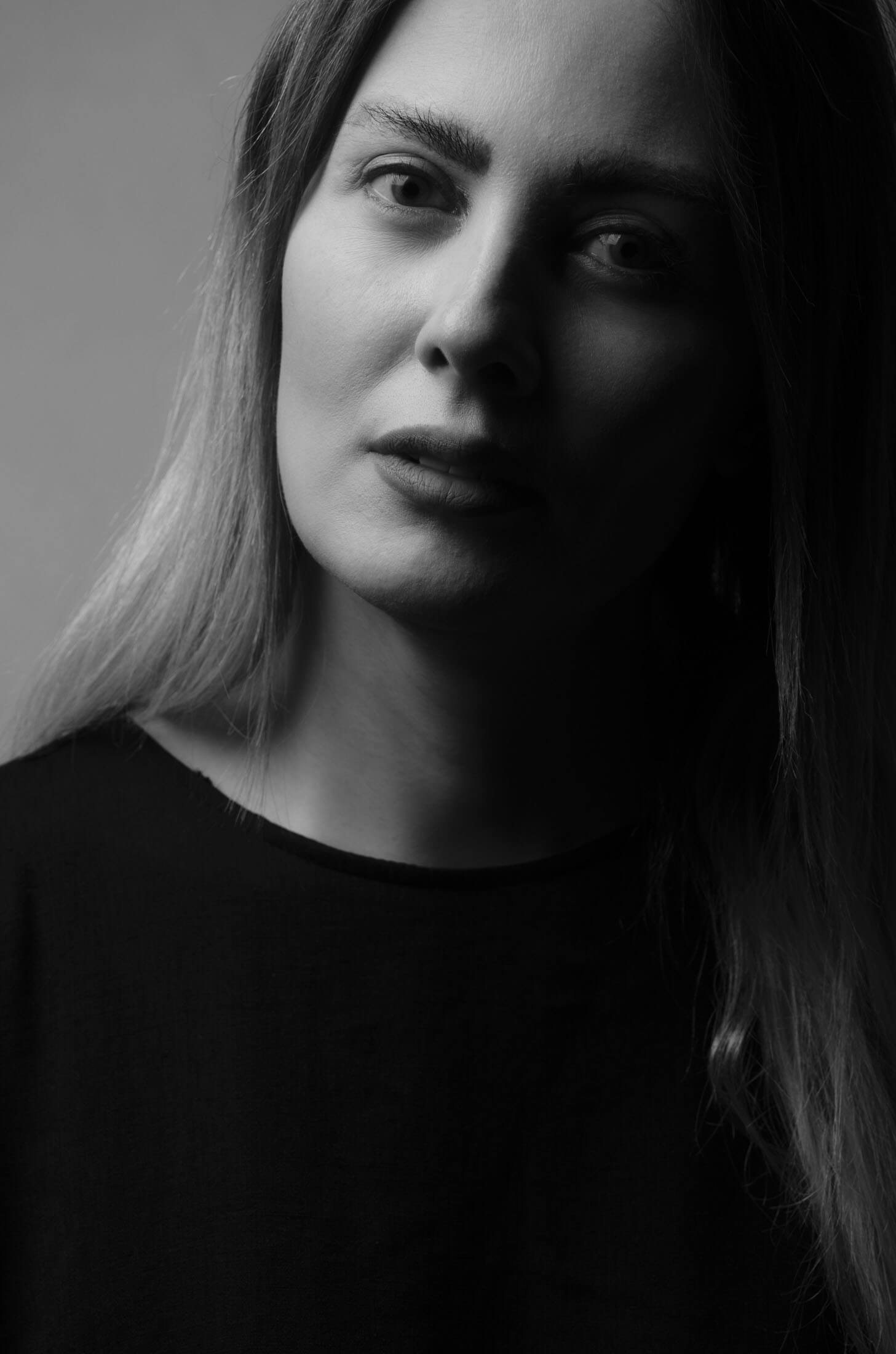 Svartvitt headshot taget av fotograf i Stockholm där ansiktet framträder ur mörker med dramatisk sidobelysning som skapar kontrast mellan ljus och skugga.