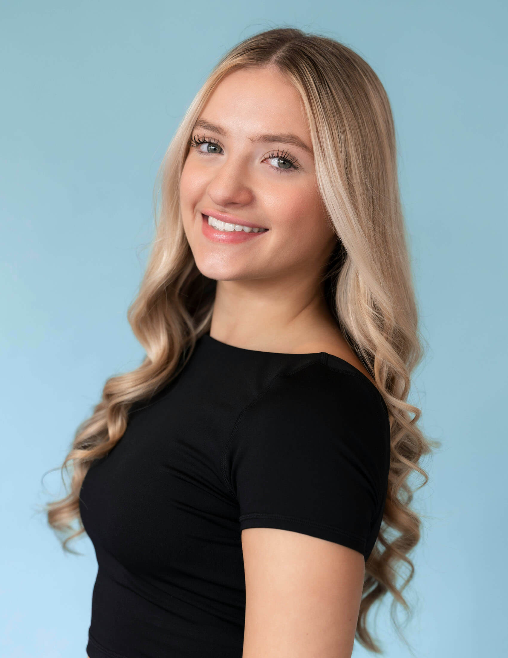 Headshot i studio taget av studiofotograf i Stockholm där person med långt blont hår står lätt vinklad mot kameran och ler. Den ljusblå bakgrunden och den mjuka ljussättningen skapar ett professionellt och inbjudande porträtt.