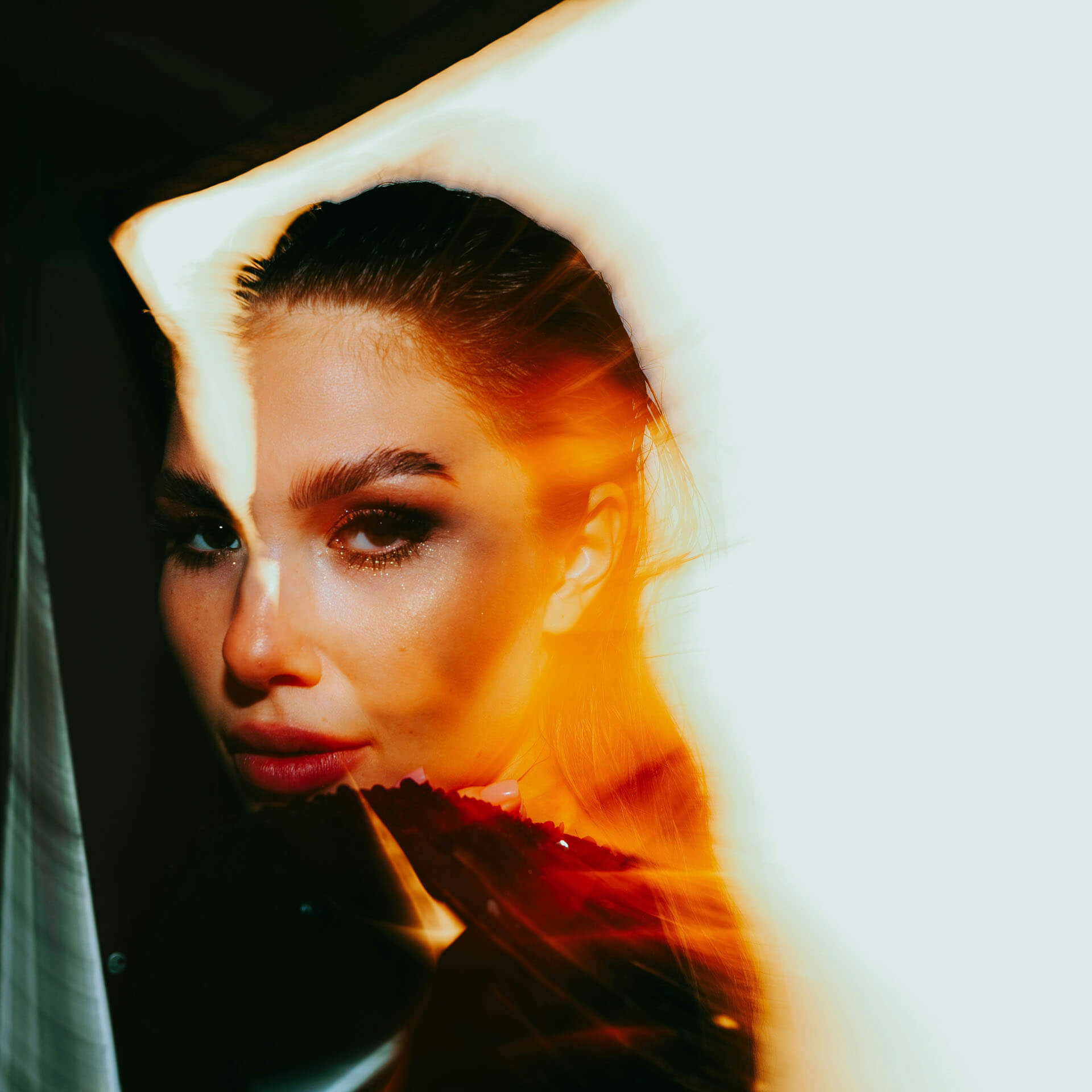High fashion-fotografering i Stockholm där ansiktet delvis täcks av färgade ljuseffekter i orange och ljusblåa toner. Den kreativa ljussättningen framhäver makeup, blick och modekänsla i ett professionellt modellfoto.