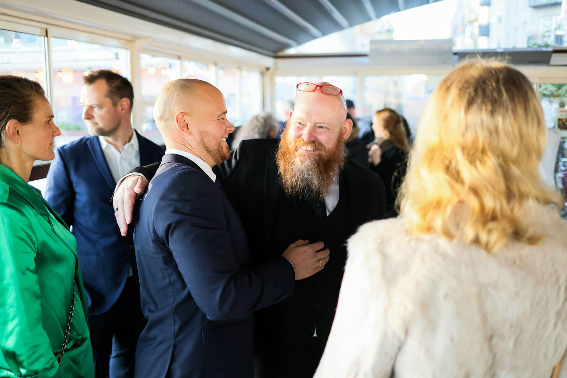 Grupp människor samtalar och umgås vid ett företagsevent inomhus, fotograferat i naturligt ljus med mjuk bakgrundsoskärpa.