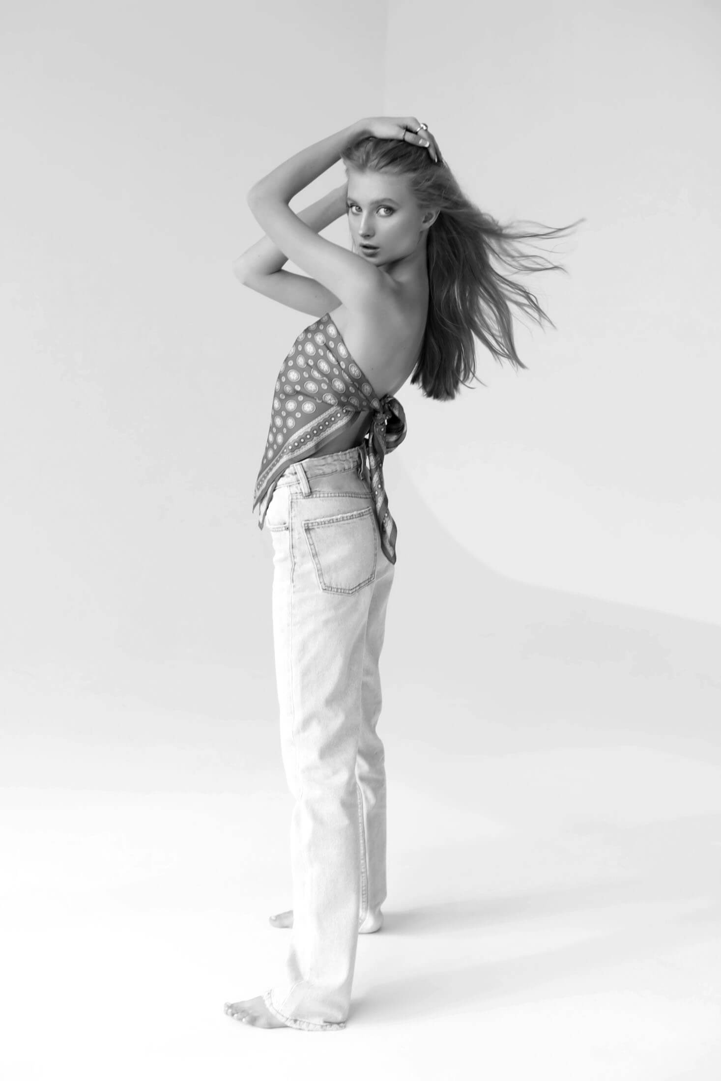 Fashionfotografering i studio i Stockholm där en kvinna poserar med händerna i håret och blicken riktad mot kameran. Den vridna kroppshållningen och håret i rörelse skapar ett uttrycksfullt modellfoto i svartvitt.