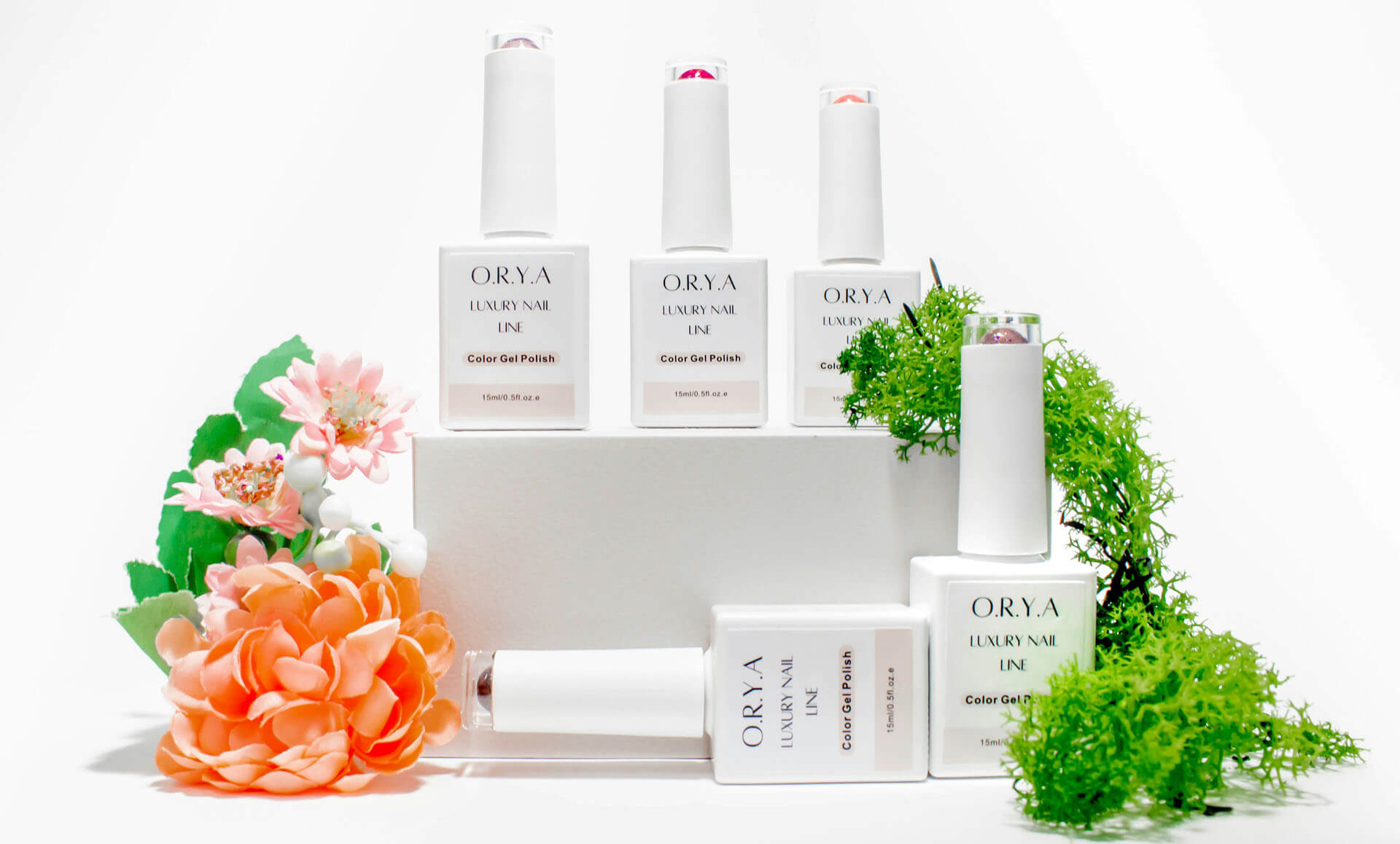 Produktfotografering i Stockholm där vita nagellacksflaskor och produktförpackningar är arrangerade på vita piedestaler i olika höjder. Orange och rosa blommor samt grön växtlighet omger produkterna och förstärker känslan av en sommarkollektion. Den ljusa studiomiljön ger en stilren produktbild för e-handel och marknadsföring