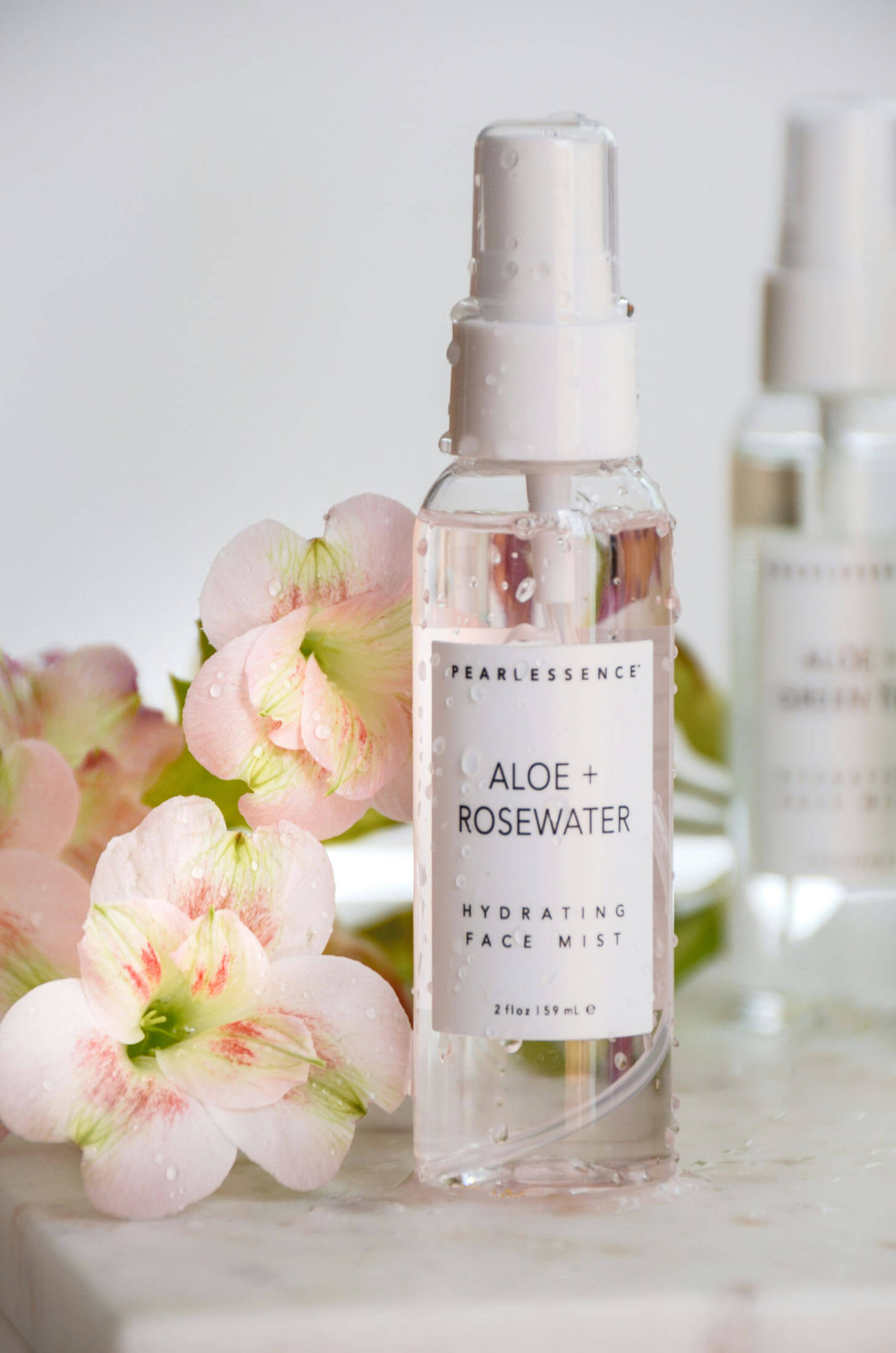 Produktfoto taget av fotograf i Stockholm där en flaska ansiktsmist står i fokus framför mjukt suddiga blommor i ljusa toner gulvita toner. Den ljusa bakgrunden och den stilrena kompositionen framhäver produktens design och skapar en fräsch och exklusiv produktbild för e-handel och marknadsföring.