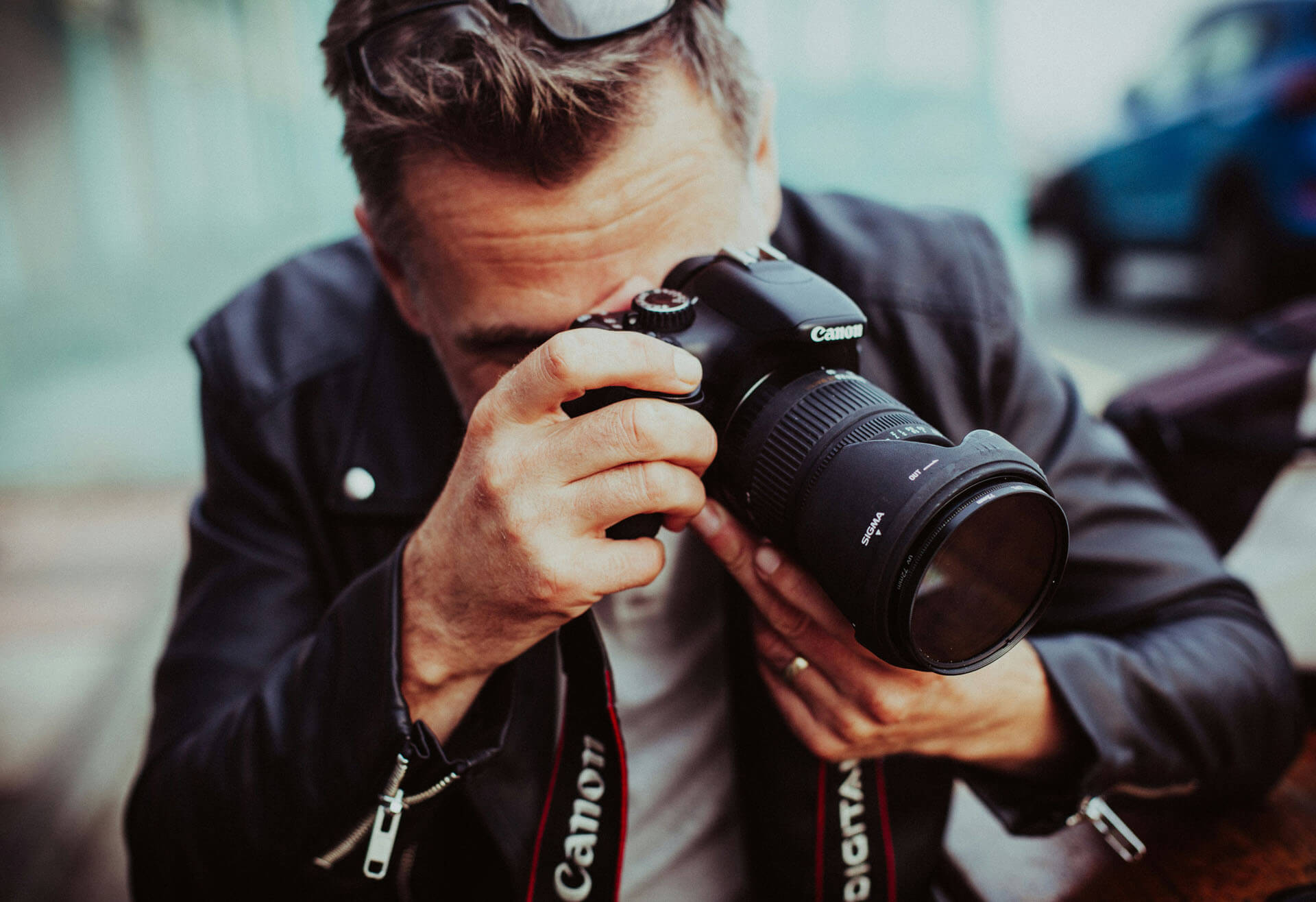 Närbild av person som håller upp en systemkamera och fotograferar, med fokus på händer, objektiv och kamerarem i naturligt ljus.