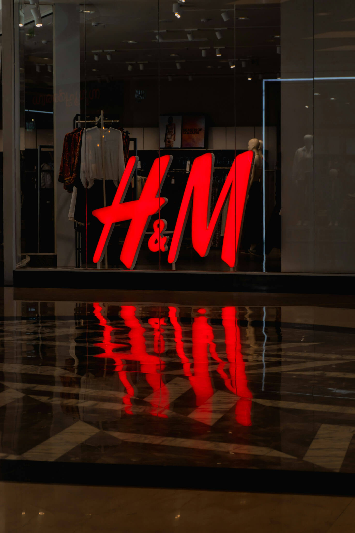 H&M-butik fotograferad som en del av varumärkesfotografering där den upplysta logotypen syns genom glasfasaden tillsammans med en del av butikens interiör. Bilden illustrerar reklamfoto och kommersiell fotografering för detaljhandel.