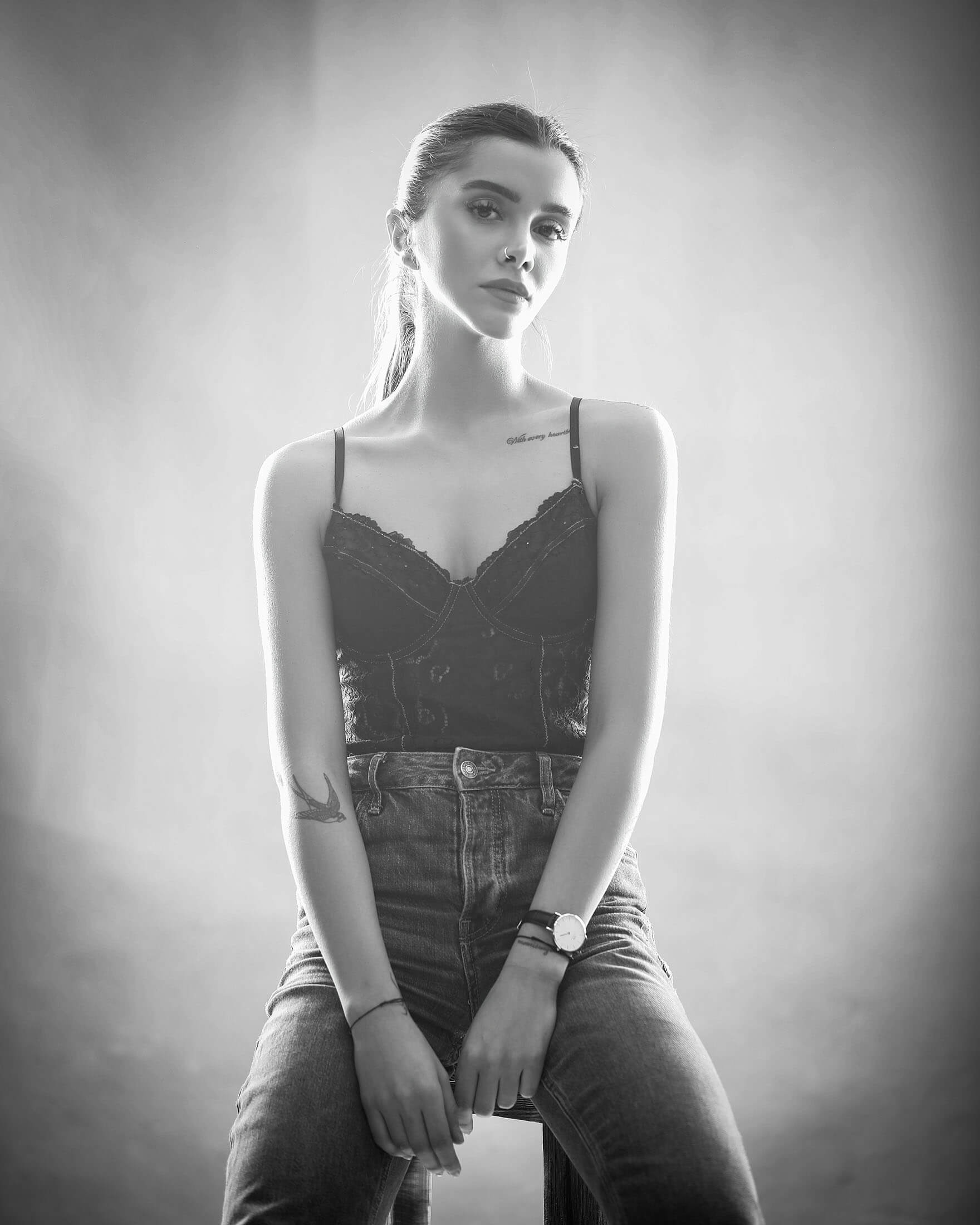 Svartvitt porträtt från TFP-fotografering i studio i Stockholm där person sitter på en stol i linne och jeans. Det mjuka sidoljuset skapar ett naturligt modellporträtt.