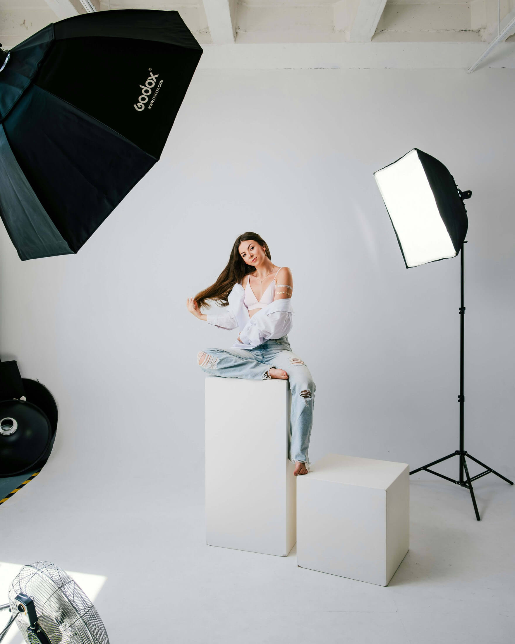 Fotostudio i Stockholm med softboxar och stativ där en person sitter på vita kuber under en professionell studiofotografering med vit bakgrund.