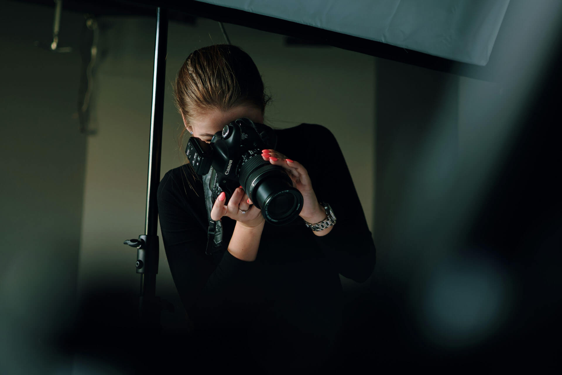Person står i en fotostudio och fotograferar med systemkamera, omgiven av ljusutrustning och mörk bakgrund som skapar en fokuserad arbetsmiljö.